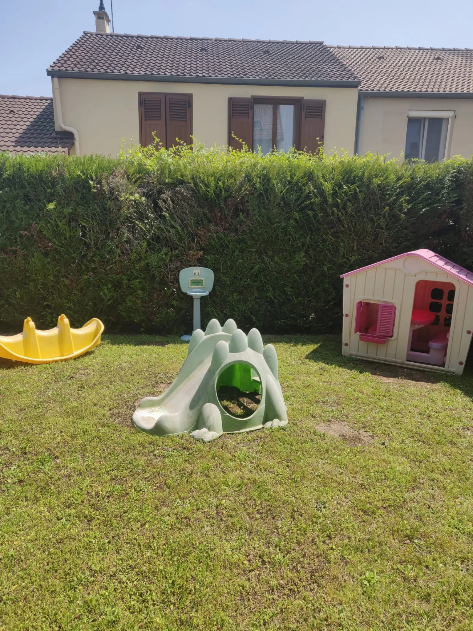 Jardin extérieur avec toboggan, maisonnette, panier de basket et trébuchet à bascule.