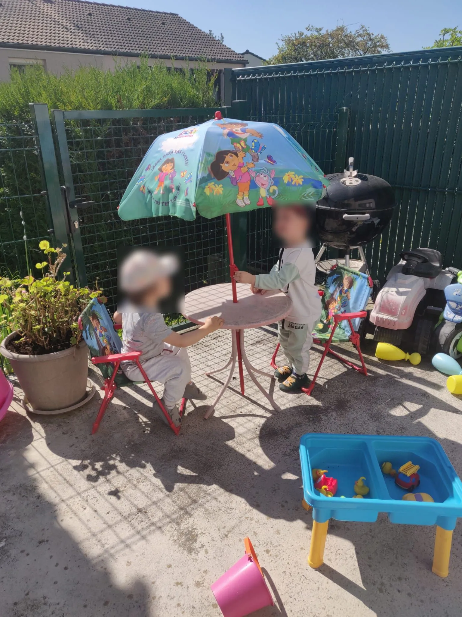 Deux enfants installés sur un salon de jardin pour enfants jouent sur la terrasse sécurisée.
